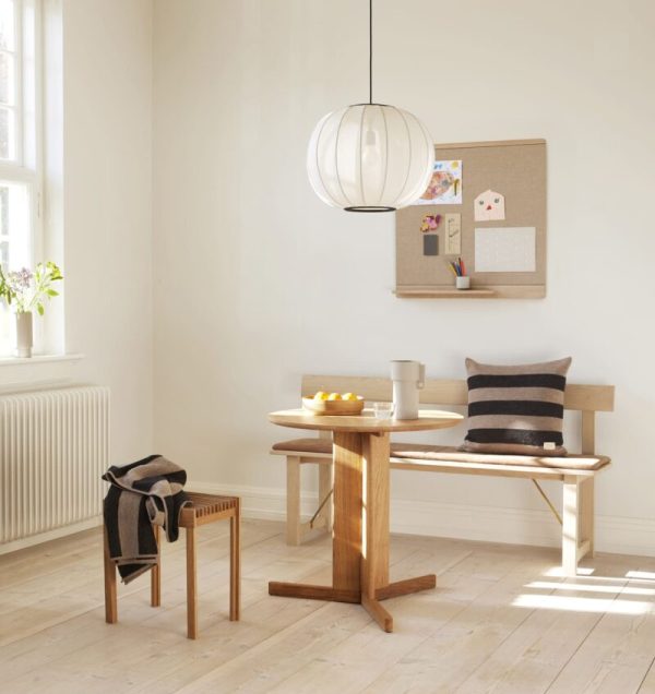 En hyggelig spisekrog med træbord og bænk, en FORM & REFINE - Position Læderhynde 155 pude og en moderne pendel. en opslagstavle hænger på væggen, og et stort vindue giver naturligt lys.