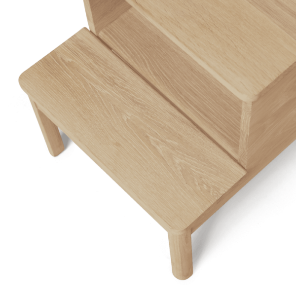 En minimalistisk trinstol i lyst træ med to niveauer, placeret på en sort overflade. Taburetten har et enkelt, funktionelt interiørdesign med afrundede kanter.