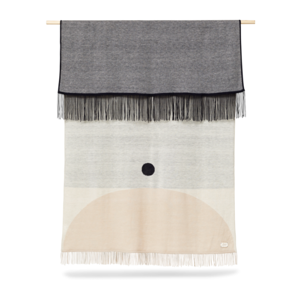 Et vægophæng med et minimalistisk design med geometriske former i neutrale toner er ophængt i en trædyvel og har frynsede kanter. FORM & REFINE - Aymara Plaid Mønster 190x130 inkluderer en sort cirkel på en beige og grå baggrund.