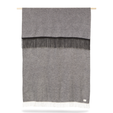 A FORM & REFINE - Aymara Plaid Moulinex 130x190 med kvaster hængende fra en træstang mod en hvid baggrund. tæppet har en frynser foroven og forneden.