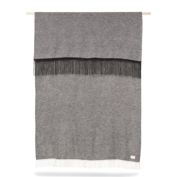 A FORM & REFINE - Aymara Plaid Moulinex 130x190 med kvaster hængende fra en træstang mod en hvid baggrund. tæppet har en frynser foroven og forneden.