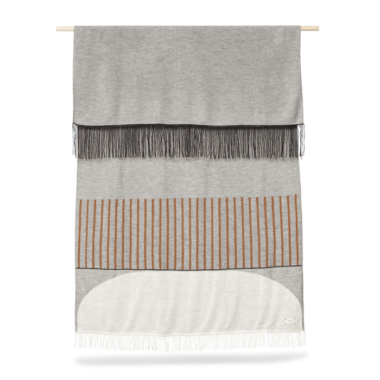 A FORM & REFINE - Aymara Plaid Mønster 190x130 væghængende gobelin med grå og hvide sektioner med en stribe af orange-brun. Tapetet har frynsede ender og hænger fra en trædyvel.