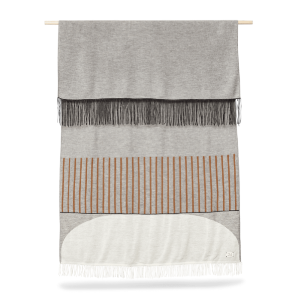 A FORM & REFINE - Aymara Plaid Mønster 190x130 væghængende gobelin med grå og hvide sektioner med en stribe af orange-brun. Tapetet har frynsede ender og hænger fra en trædyvel.