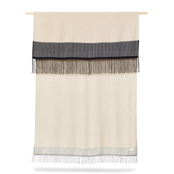 A FORM & REFINE - Aymara Plaid Stripes 190x130 vægophæng med en cremefarvet base med vandrette sorte og grå striber øverst og nederst, suppleret med frynsede kanter, vist på en træstang.