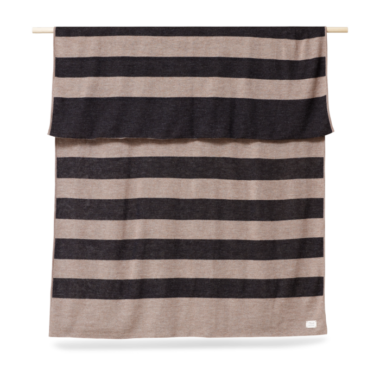 A FORM & REFINE - Aymara Plaid Ribbon 190x130 i skiftevis beige og brune striber hænger mod en almindelig baggrund og viser et ligetil og moderne design.