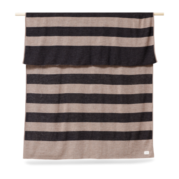 A FORM & REFINE - Aymara Plaid Ribbon 190x130 i skiftevis beige og brune striber hænger mod en almindelig baggrund og viser et ligetil og moderne design.