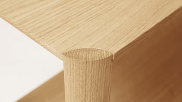 Nærbillede af en FORM & REFINE - Leaf Reol 1x2, der viser den glatte tekstur af bordpladen og det afrundede hjørne med et cylindrisk ben, der fremhæver træets årer og naturlige finish.