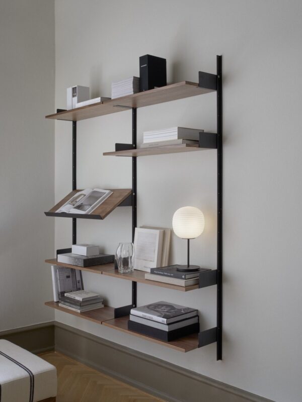 En moderne vægmonteret reol med sorte lodrette understøtninger og fem træhylder, dekoreret med bøger, et indrammet foto, en sfærisk lampe og minimalistisk indretning i et neutralt tonet rum af TomorrowsDesign.
