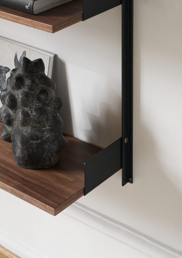 En unik stenskulptur, der ligner et stiliseret hoved placeret på en træhylde, understøttet af sorte metalbeslag mod en hvid væg, der viser moderne interiørdesign.