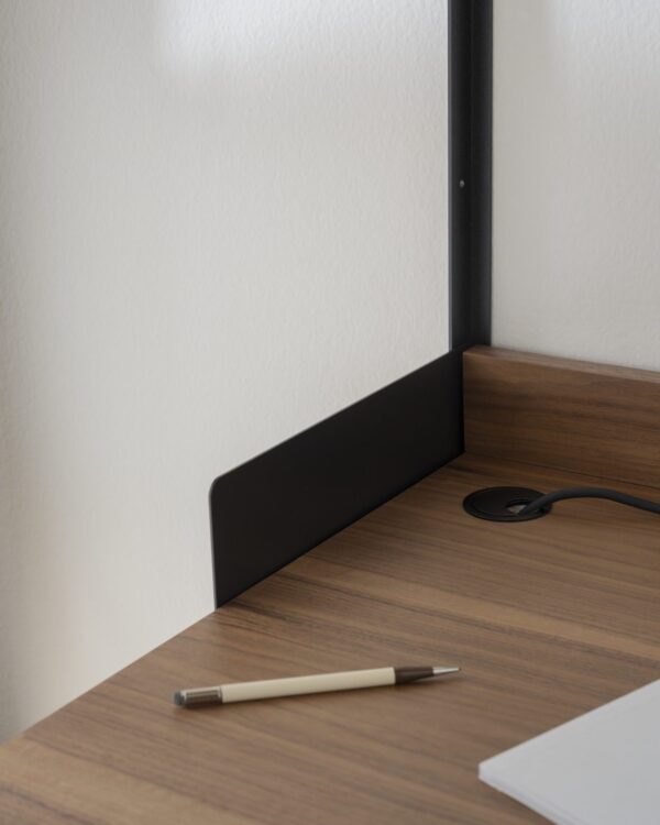 Et minimalistisk arbejdsområdehjørne med et træskrivebord, med en sort laptop-forhøjer og en biro pen ved siden af en hvid væg. En delvist synlig notebook og netledning vises også i scenen. Denne opsætning repræsenterer perfekt TomorrowsDesign-etoset.