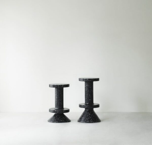 To NORMANN COPENHAGEN - Bit Barstol 75 taburetter står mod en almindelig, lysegrå baggrund og viser et symmetrisk design med cylindriske sæder og udstrakte baser.