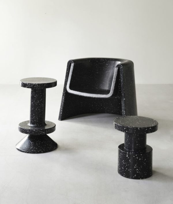 En sort NORMANN COPENHAGEN - Bit Barstol 65 lænestol og tre matchende cylindriske taburetter sat på en almindelig lysegrå baggrund. Møblerne har et spættet mønster og moderne design.