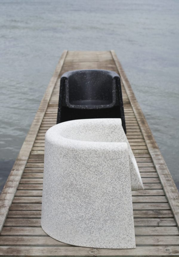 En overskyet dag på en sø med en smal trædok, med to NORMANN COPENHAGEN - Bit Loungestol stole - en sort og en hvid med et glat, kurvet design, der sidder ud mod vandet.