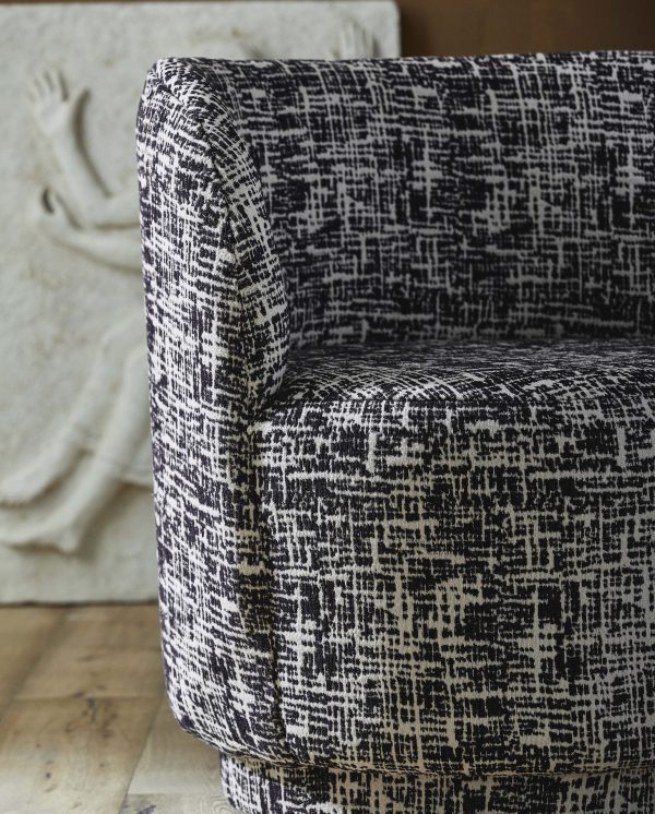 Et nærbillede af en lænestol betrukket med sort og hvid tweedstof, med fokus på materialets tekstur og mønster. baggrunden sløres blødt og antyder en neutral skulptur.