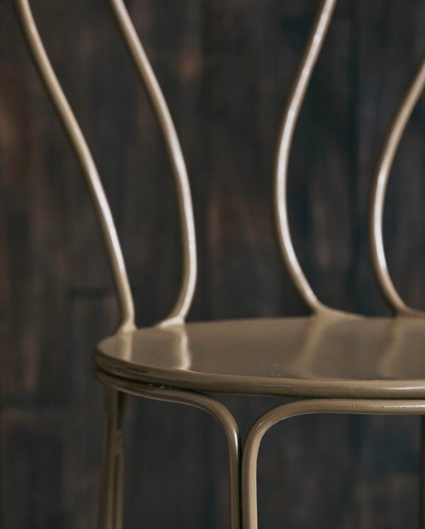 Nærbillede af en metalstol med elegant buet ryglæn mod en tekstureret mørkeblå baggrund. fokus er på stolens håndværk og designdetaljer.