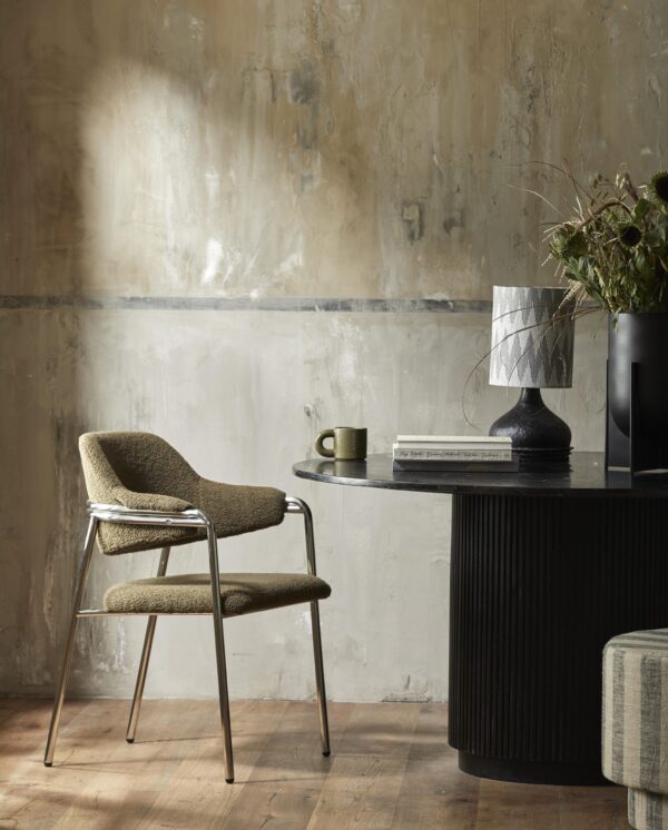 Minimalistisk interiør med et rundt sort bord og en tekstureret stol ved siden af. rummet er indrettet med vase, lampe og planter på bordet, sat op ad en rustik væg.