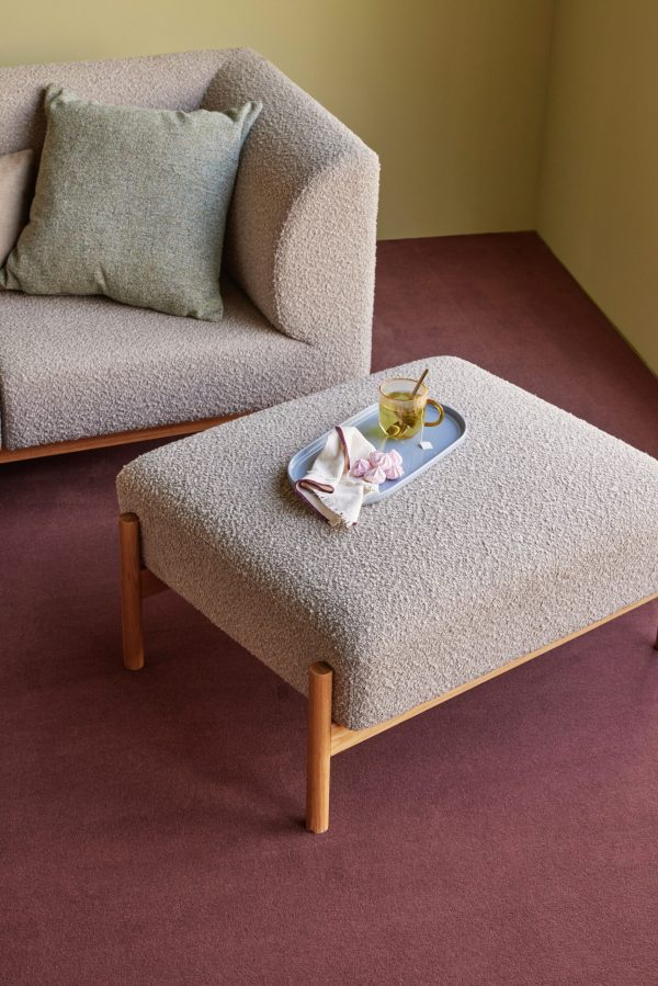 Et elegant, hyggeligt stuehjørne med en sherpabeklædt lænestol ved siden af en matchende skammel. skammel holder en serveringsbakke med en tekop og en krøllet serviet. rige, dybrøde og grønne vægge omslutter rummet.