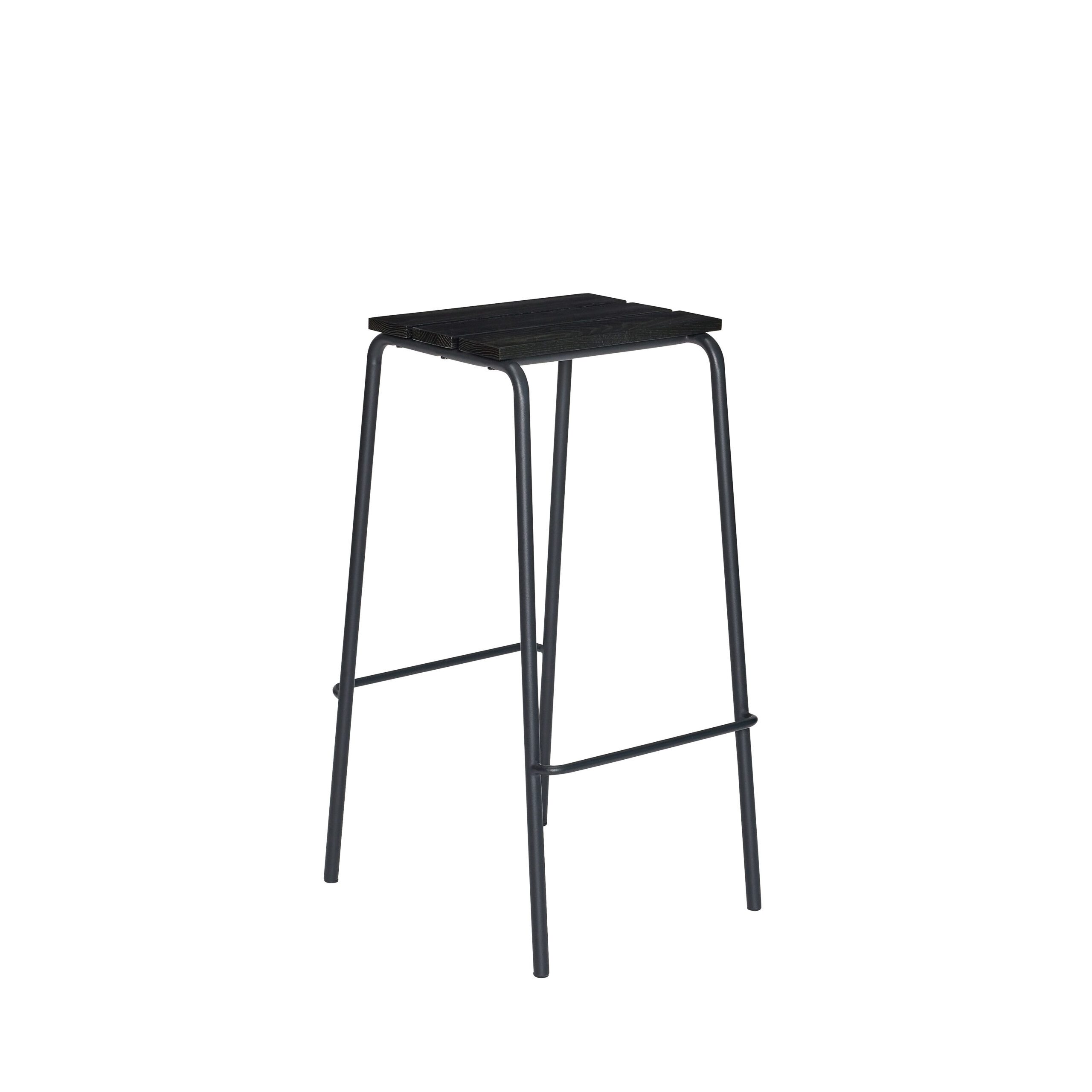 En sort metal barstol med et minimalistisk design og fire slanke ben, med et firkantet, tekstureret sæde og en fodstøtte. skamlen er sat mod en almindelig hvid baggrund.