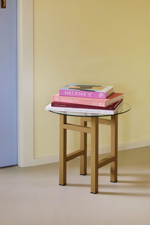 Et lille træbord står op ad en pastelgul og blå væg og rummer en stak af tre store kunstbøger med den øverste titlen "hockney". indstillingen er enkel og rolig.