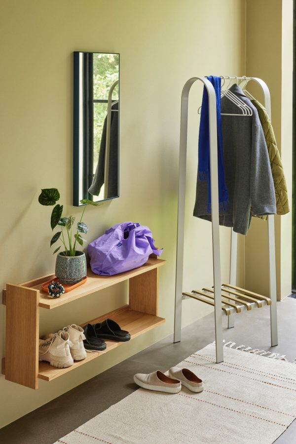 En moderne entré med en træbænk med opbevaring til sko, en knageholder med hængende jakker, et spejl på væggen og dekorative planter. rummet har grønne vægge og et beige tæppe.
