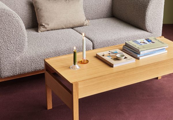 En moderne stue med en lysegrå sofa med en beige pude, et sofabord i træ med bøger, en lysestage med to tændte stearinlys og et lille fad. rummet har et lilla tæppe og blød belysning.
