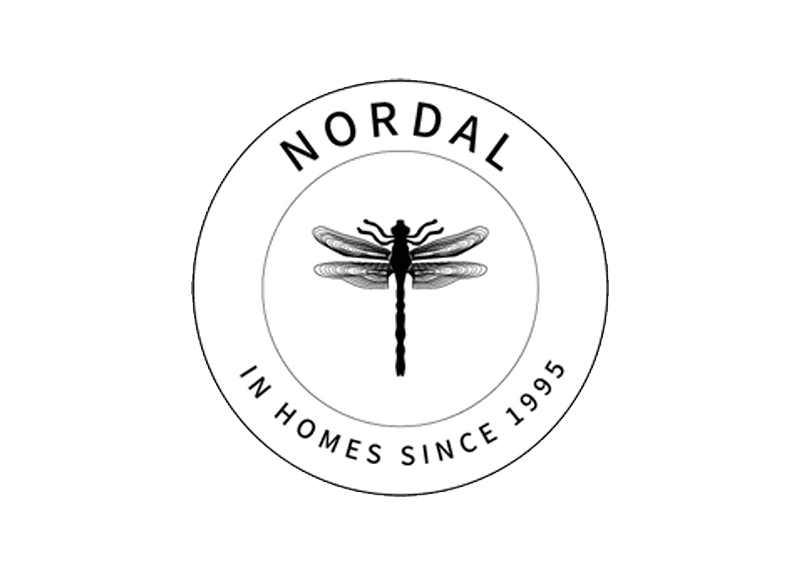 Billedet viser et cirkulært logo for mærket "Nordal." I midten er en detaljeret illustration af en guldsmede. Teksten "NORDAL" er buet langs den øverste kant, og sætningen "I boliger siden 1995" er buet langs den nederste kant.