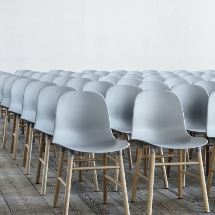 Rækker af moderne grå stole med træben, designet af TomorrowsDesign, pænt afstemt i et rummeligt værelse med lyst trægulv og hvid vægbaggrund.